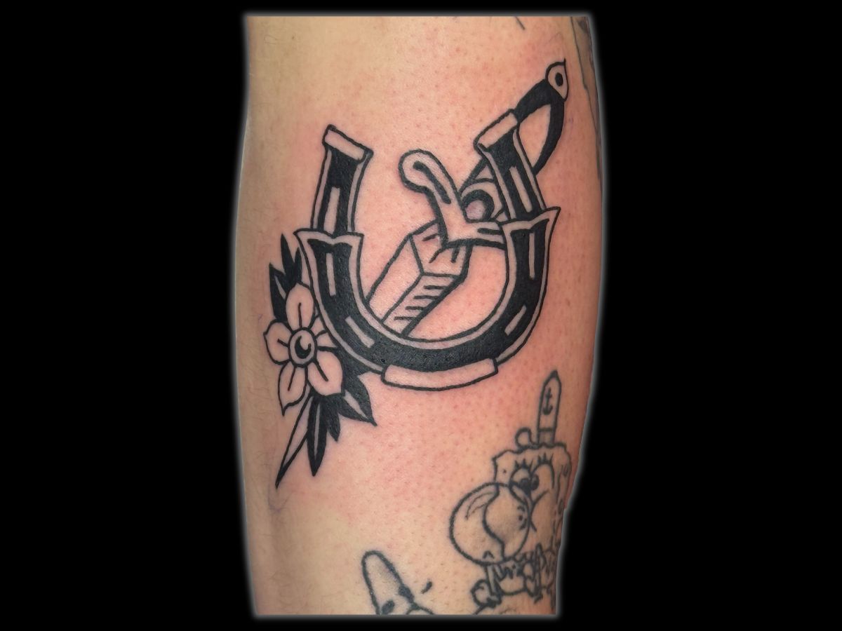 Dagger and horseshoe tattoo by Robert — classic good luck motif in bold lines.